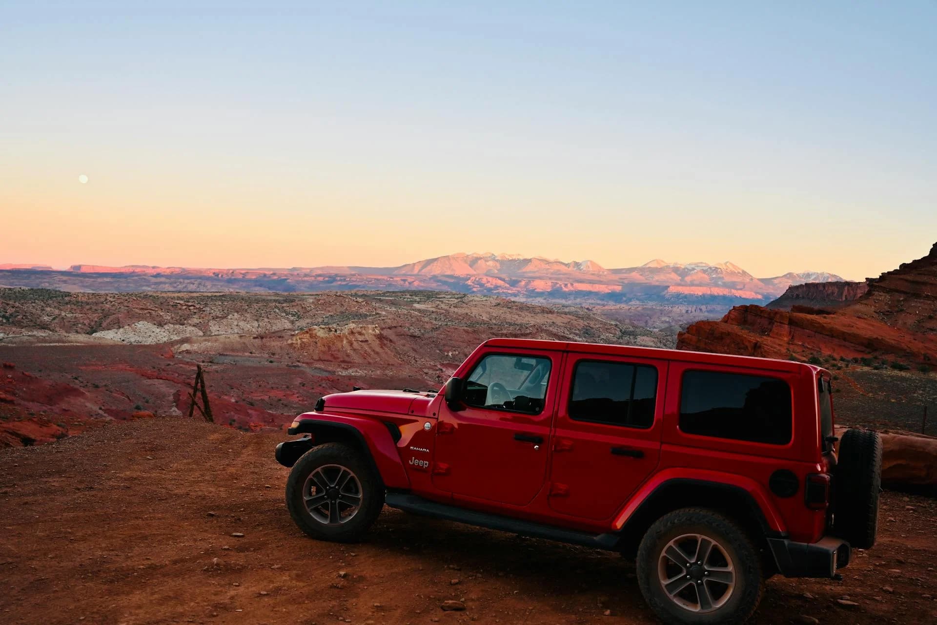 Red Jeep Wrangler at sunset in Moab, Utah with snow-capped mountains